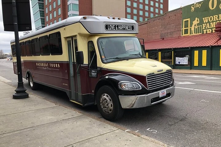 Een rood met beige toerbus van Backbeat Tours staat geparkeerd langs een straat in Memphis met winkelpanden op de achtergrond