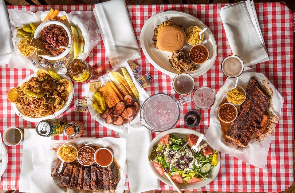 Bovenaanzicht van een tafel vol gerookte ribben, coleslaw, bonen en drankjes op een roodwit geblokt tafelkleed in het Rendezvous restaurant in Memphis
