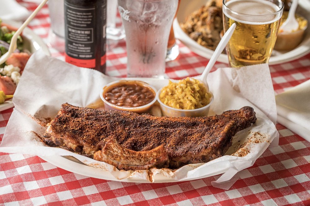 Bord met droog gekruide gerookte ribben, gebakken bonen en maissalade naast een glas bier op een roodwit geblokt tafelkleed in Memphis