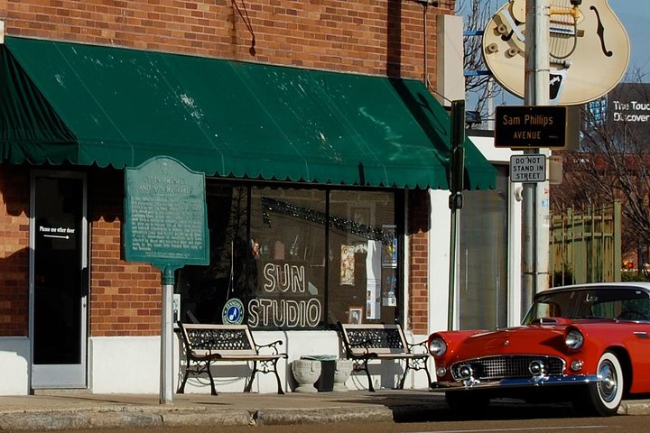 Bakstenen gevel van het beroemde Sun Studio in Memphis met een groene luifel, bankjes en een rode klassieke auto op straat