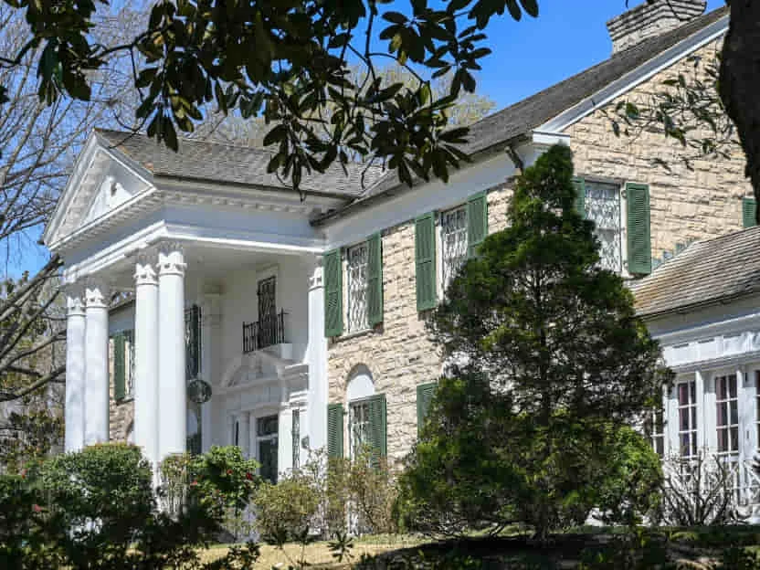 Het statige herenhuis Graceland in Memphis met witte zuilenportiek, groene luiken en groen aan de gevel omgeven door bomen