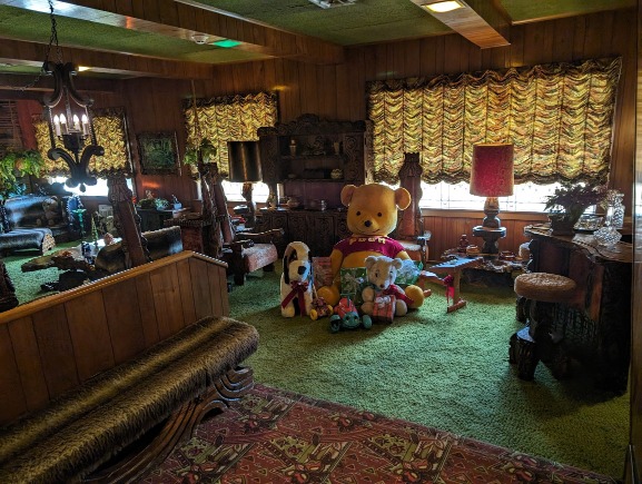 Kamer met groen tapijt op vloer en plafond, houten meubels met dierenmotieven en knuffels in de Jungle Room van Graceland in Memphis