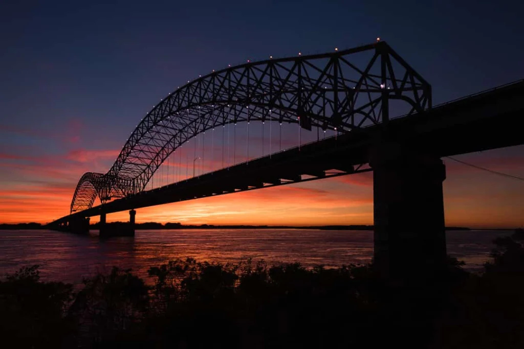 De stalen boogbrug over de Mississippi kleurt donker af tegen een felle oranje lucht bij zonsondergang in Memphis