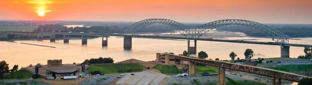 Boogbrug over de brede Mississippi rivier bij Memphis, gefotografeerd vanaf de oever bij een gloeiende zonsondergang