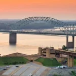 Boogbrug over de brede Mississippi rivier bij Memphis, gefotografeerd vanaf de oever bij een gloeiende zonsondergang