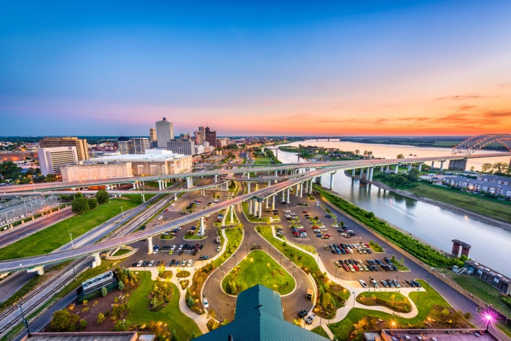 Luchtfoto van het centrum van Memphis met een verlicht snelwegknooppunt, een parkeerterrein en de rivier op de achtergrond bij schemering