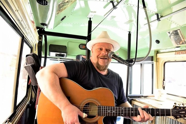 Lachende muzikant met hoed zingt en speelt akoestische gitaar in een tourbus met groen interieur in Memphis
