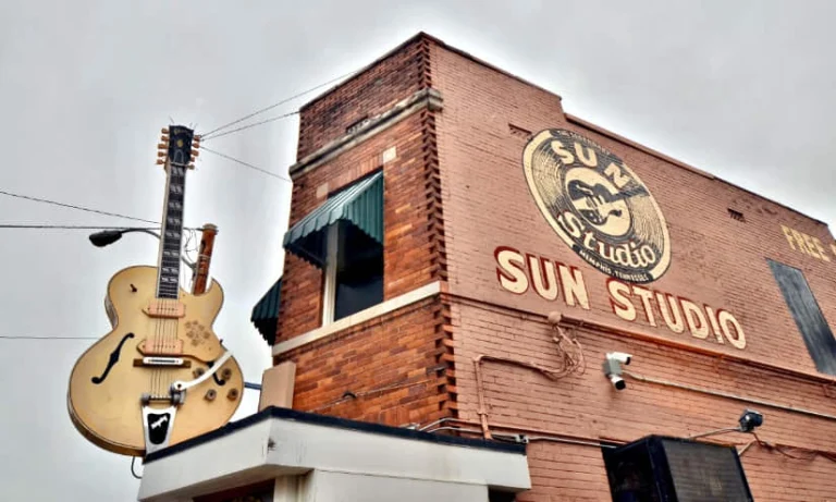 Een grote gouden gitaar hangt aan de bakstenen gevel van het beroemde Sun Studio in Memphis onder een bewolkte hemel