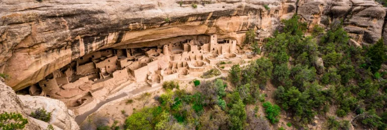 Uitzicht op de oude rotswoningen van Mesa Verde National Park, gebouwd onder een grote rotsoverhang omringd door groene begroeiing