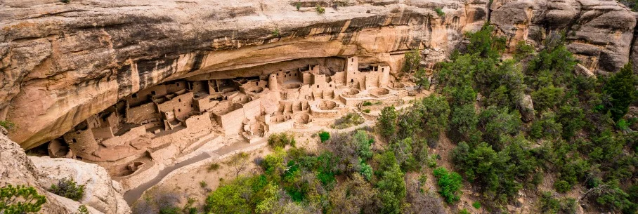 Uitzicht op de oude rotswoningen van Mesa Verde National Park, gebouwd onder een grote rotsoverhang omringd door groene begroeiing