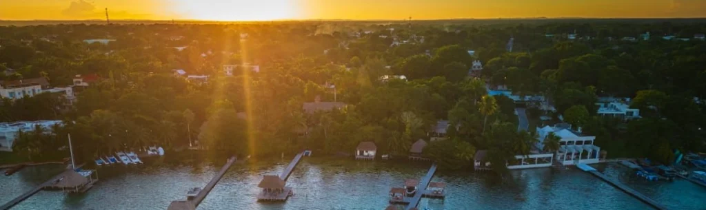 Luchtfoto van meerdere steigers die uitsteken in een lagune terwijl de zon oranje onder gaat bij Bacalar