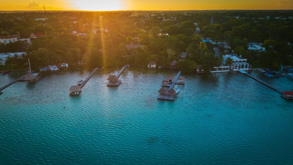 Luchtfoto van verschillende houten steigers die de lagune van Bacalar in steken bij een gouden zonsondergang