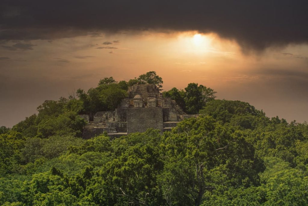 Een hoge stenen Maya piramide steekt uit boven het dichte jungle bladerdak onder een dramatische avondlucht