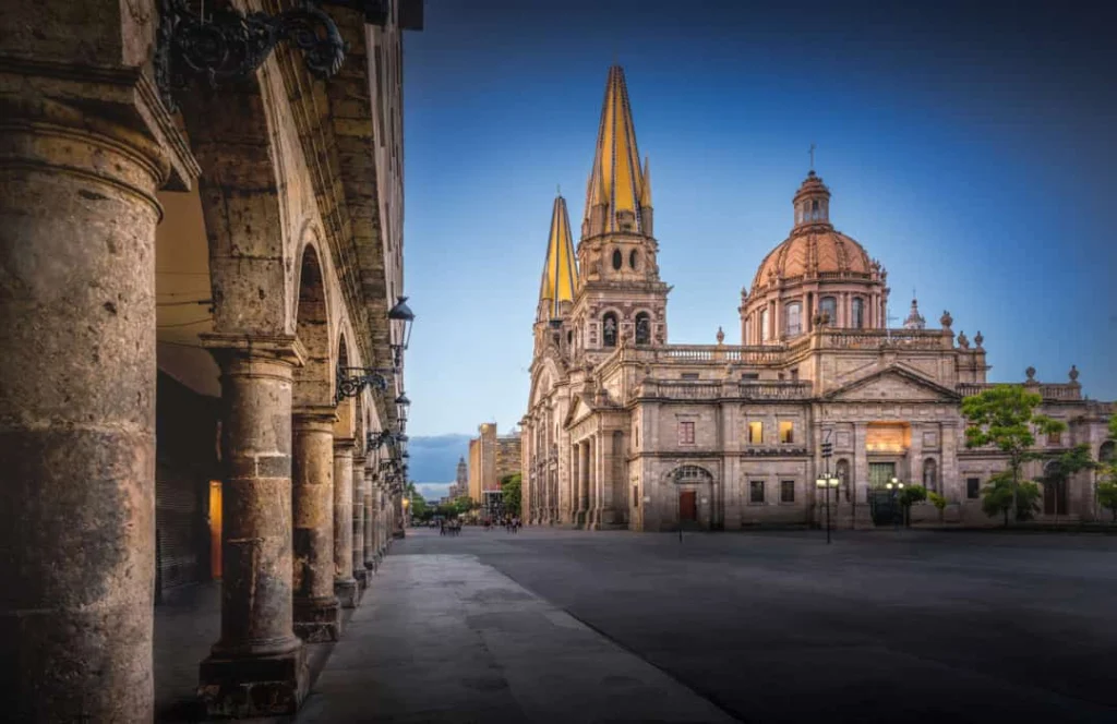 De twee gele torenspitsen van de kathedraal van Guadalajara steken uit boven het plein in de avondschemering