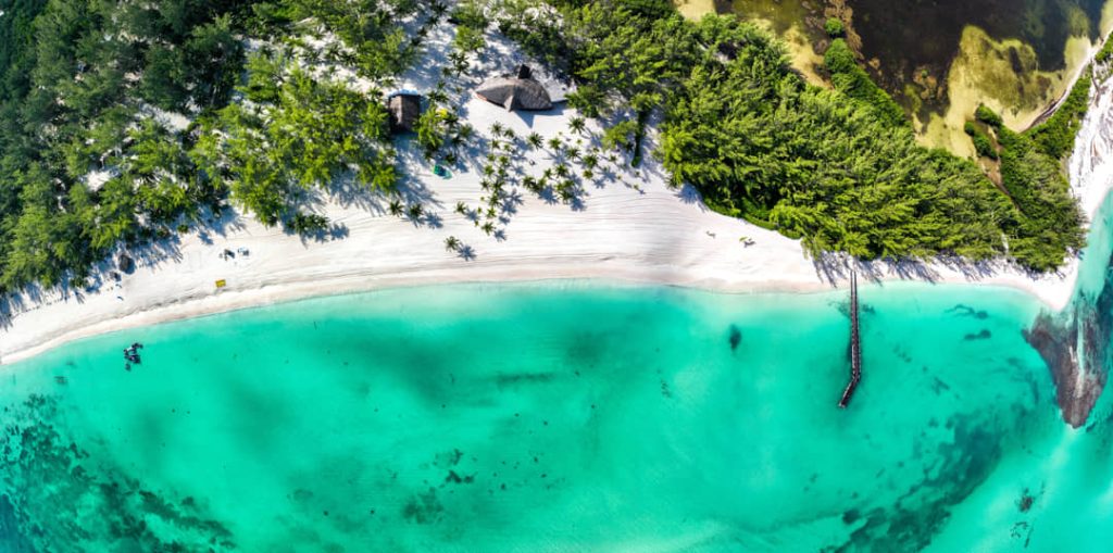 Luchtfoto van boven op een halvemaanvormige baai met wit zand, palmbomen en helder turkoois water