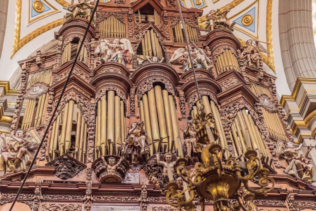 Een rijk versierd gouden kerkorgel met houten pijpen en gebeeldhouwde engelen in een barokke Mexicaanse kathedraal