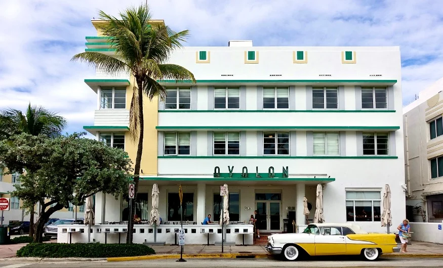 Wit en groen art deco hotel met de naam Avalon en een gele klassieke auto ervoor aan Ocean Drive