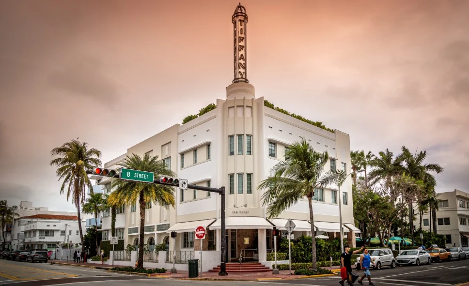 Wit art deco hotel met een hoge neonzuil en de tekst Tiffany op de hoek van Ocean Drive