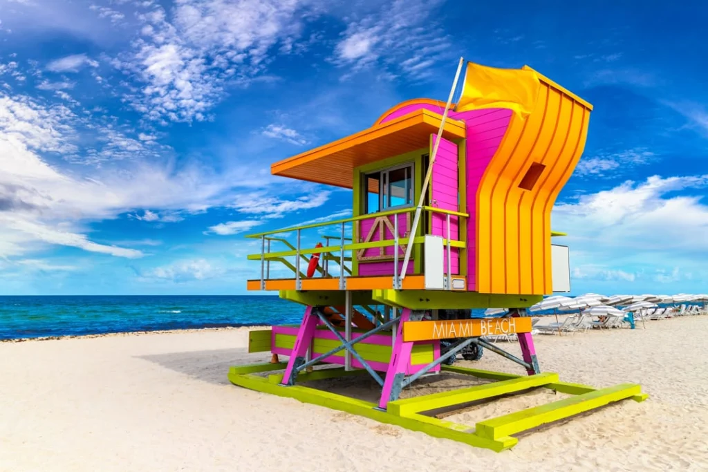 Opvallende roze, gele en oranje reddingstoren met de tekst Miami Beach op een breed zandstrand onder een blauwe lucht