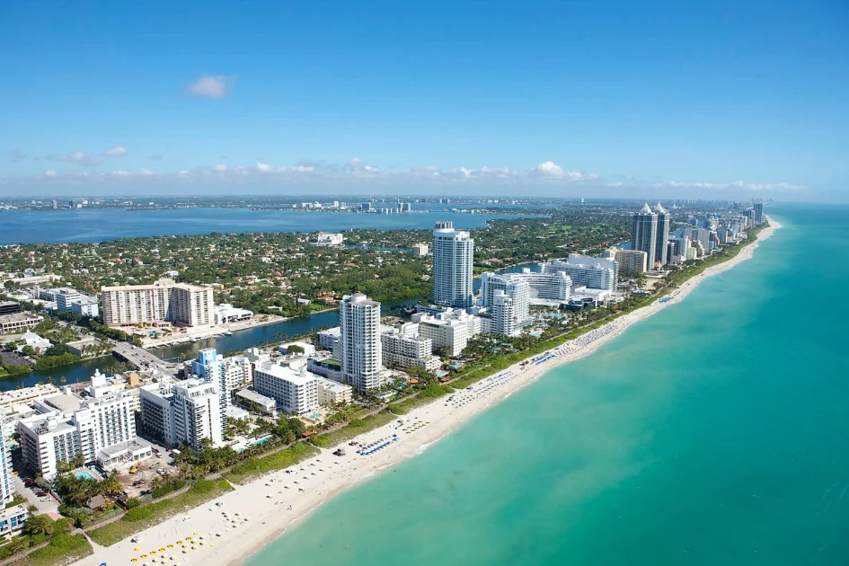 Luchtfoto van hotels en appartementen langs een breed zandstrand met turquoise zee in Miami Beach