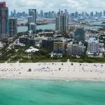 Luchtfoto van een druk zandstrand met turquoise water en de hoge gebouwen van Miami Beach op de achtergrond