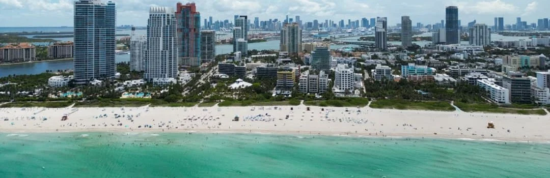 Luchtfoto van een druk zandstrand met turquoise water en de hoge gebouwen van Miami Beach op de achtergrond