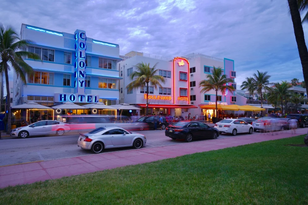 Verkeer en terrassen bij neonverlichte art deco hotels als Colony en Boulevard aan Ocean Drive in Miami Beach
