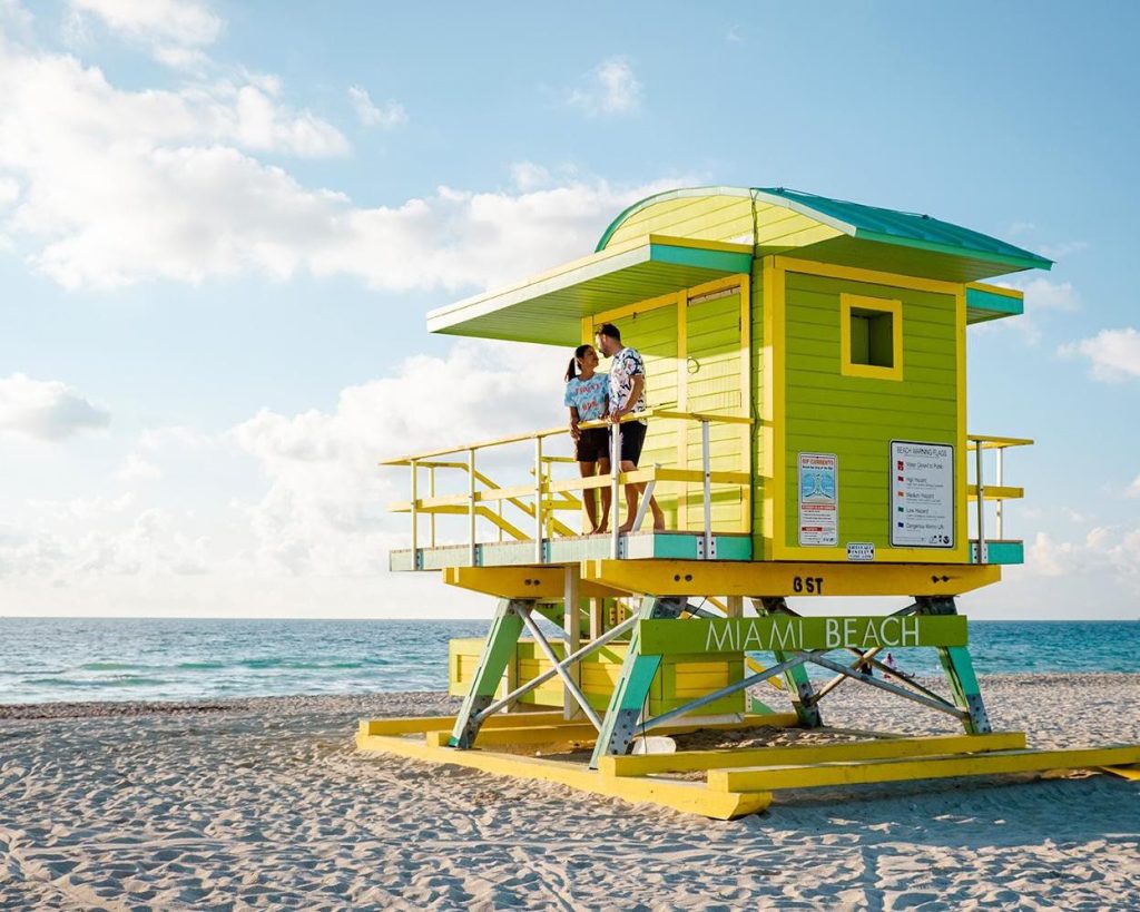 Stel staat op een groen gele reddingspost met het opschrift Miami Beach op een wit strand bij zonsopgang