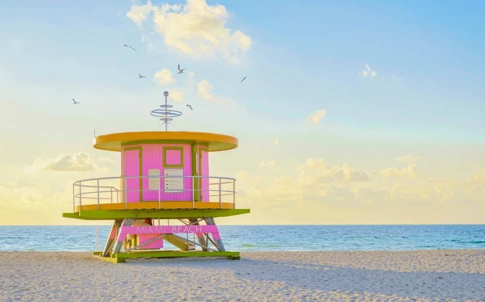 Een roze met geel reddingsstation met opschrift Miami Beach staat op het witte zand bij een rustige zee