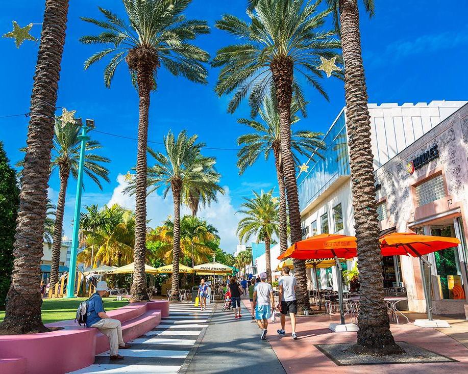 Voetgangersgebied Lincoln Road in Miami Beach met hoge palmbomen, terrassen met oranje parasols en wandelende mensen
