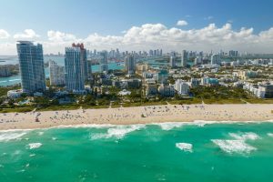 Luchtfoto van een druk zandstrand met turquoise water en de wolkenkrabbers van Miami Beach op de achtergrond