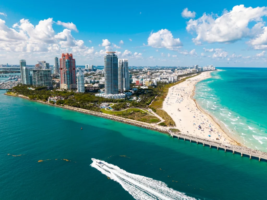 Luchtfoto van de smalle landtong van Miami Beach met wolkenkrabbers, strand en een speedboot die een spoor trekt in het water