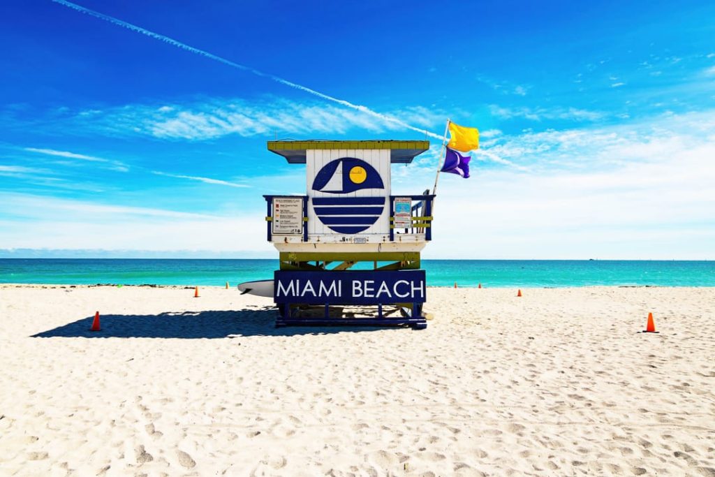 Blauw met witte reddingspost met het opschrift Miami Beach en een gele vlag op een leeg zandstrand met turquoise zee