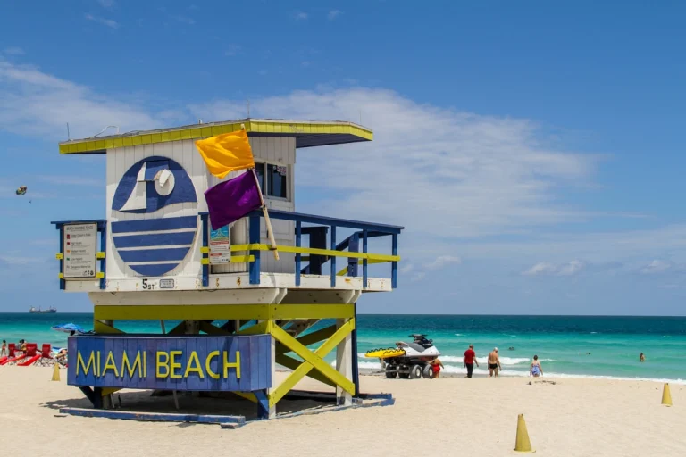 Een blauw-gele reddingspost met vlaggen op Miami Beach, met wandelaars en een waterscooter aan de vloedlijn