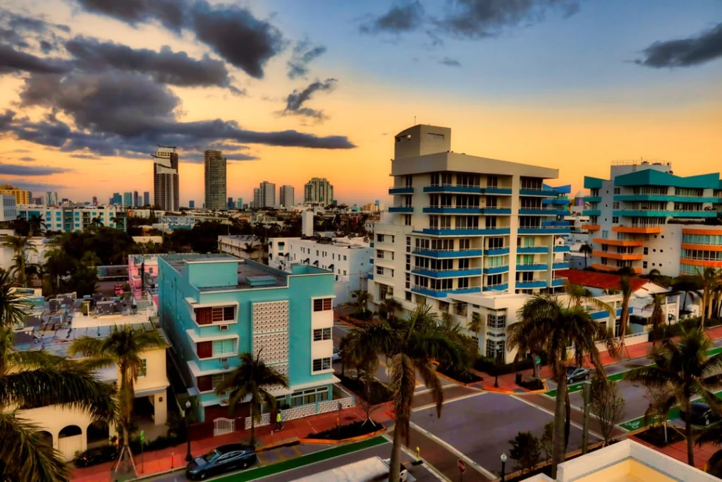 Kleurrijke art deco gebouwen en palmbomen in een woonwijk van Miami Beach met de skyline op de achtergrond bij zonsondergang