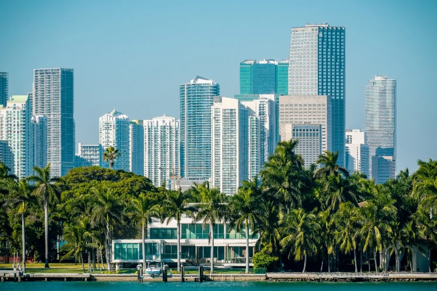 Wolkenkrabbers van downtown Miami boven een rij palmbomen, met een wit huis aan het water op de voorgrond