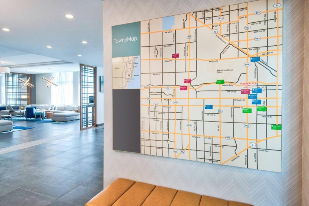 Moderne hotellobby in Miami met een grote wandkaart van de stad, gietijzeren kroonluchter en een loungehoek met bruine banken