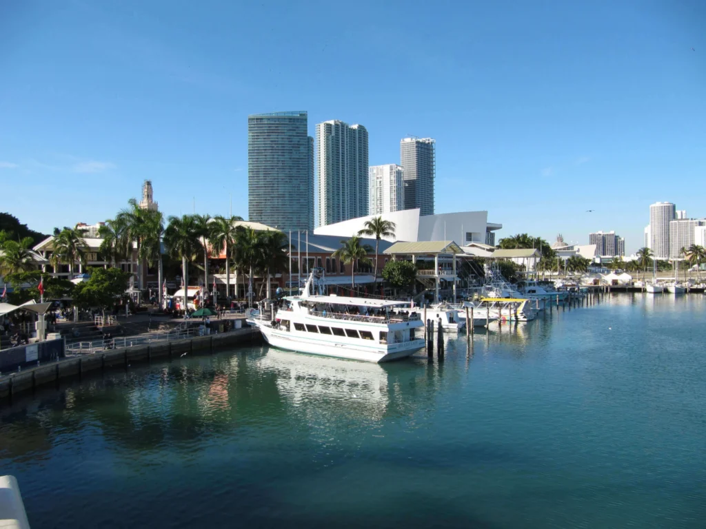 Een witte rondvaartboot en jachten liggen afgemeerd in de jachthaven bij Bayside Marketplace in Miami, met de wolkenkrabbers van downtown op de achtergrond