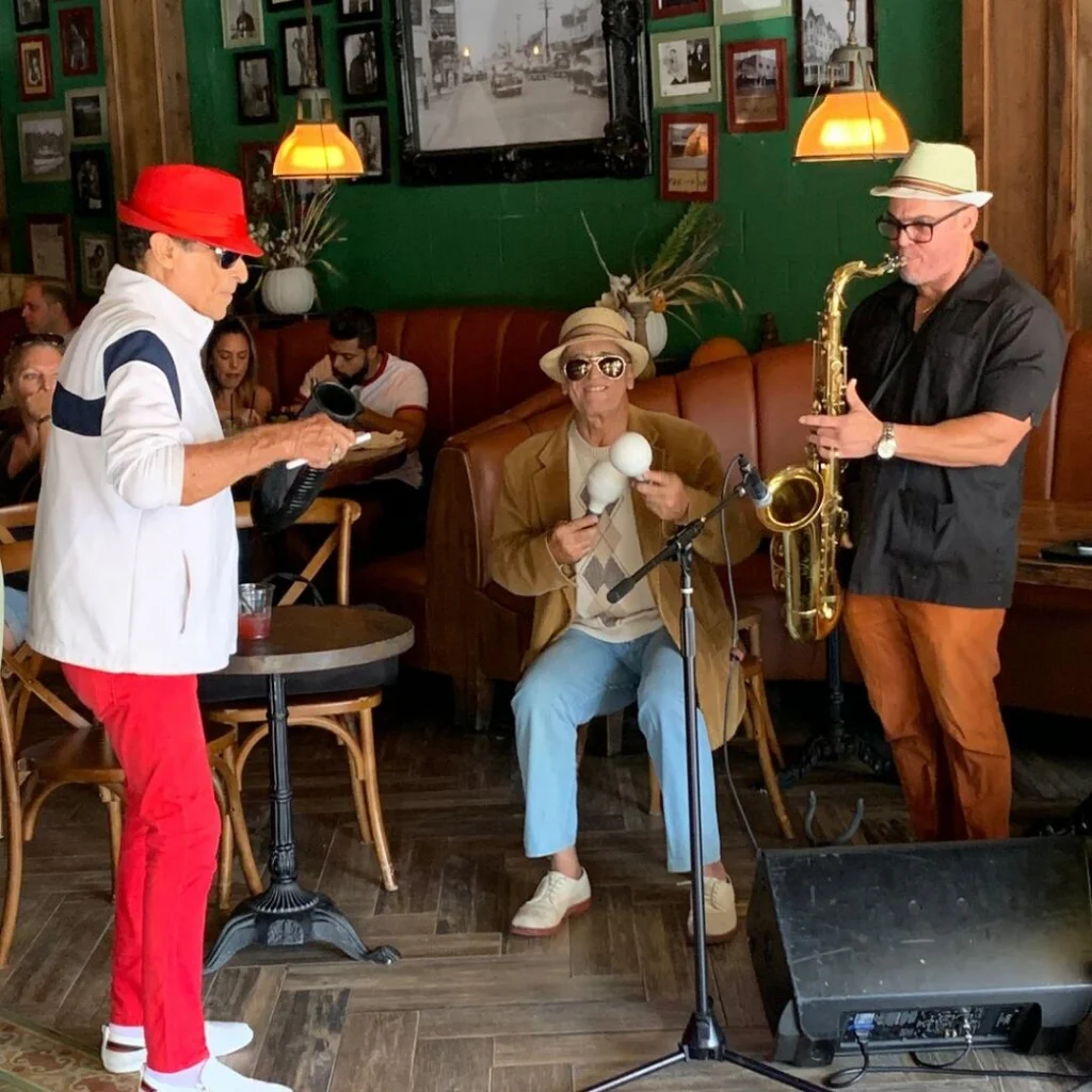 Drie muzikanten met hoeden spelen saxofoon en maracas in een sfeervol café in Little Havana, Miami