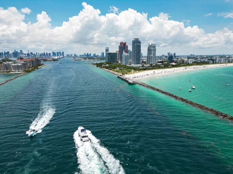 Luchtfoto van Miami met twee boten op het water, een pier en de skyline naast een turquoise strand