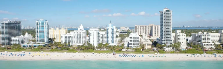 Luchtfoto van hoge witte appartementengebouwen langs het strand van South Beach in Miami met turkoois water en zonaanbidders op het zand