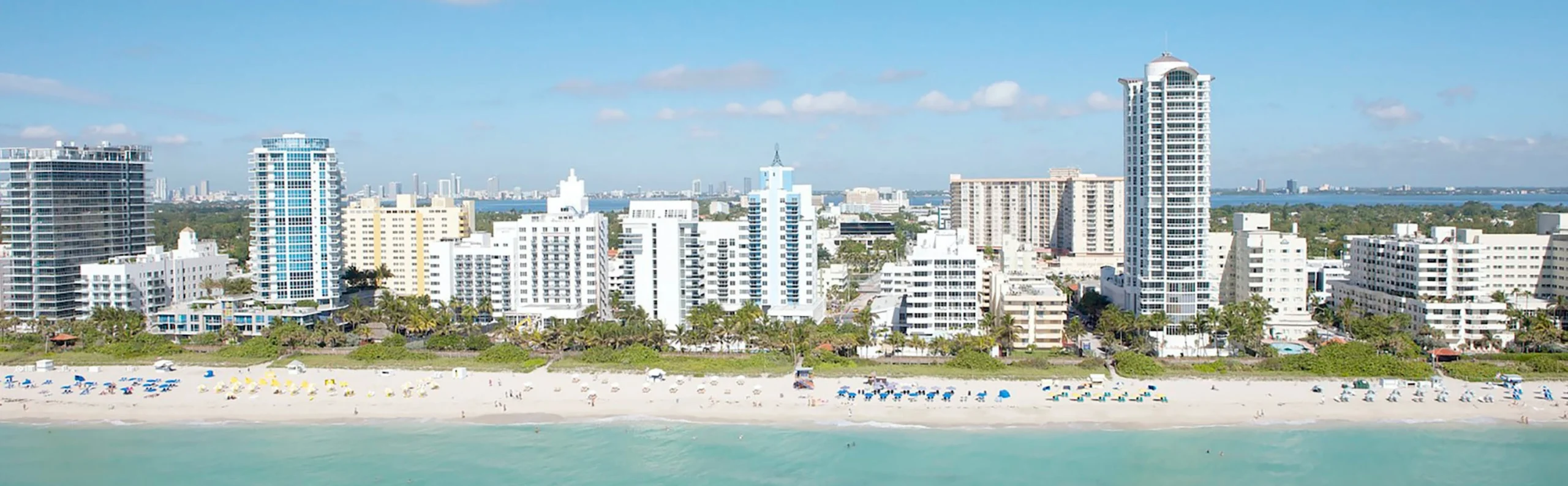 Luchtfoto van hoge witte appartementengebouwen langs het strand van South Beach in Miami met turkoois water en zonaanbidders op het zand