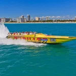 Gele speedboot met toeristen aan boord raast door het water met de skyline van Miami en het strand op de achtergrond