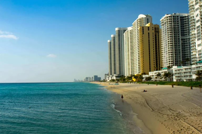 Leeg zandstrand met turquoise zee en een rij hoge appartementengebouwen langs de kustlijn bij Miami