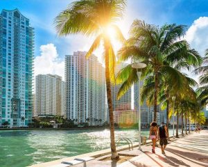 Wandelend stel op een pad langs de Miami River met palmbomen en hoge appartementengebouwen die oplichten in de namiddagzon