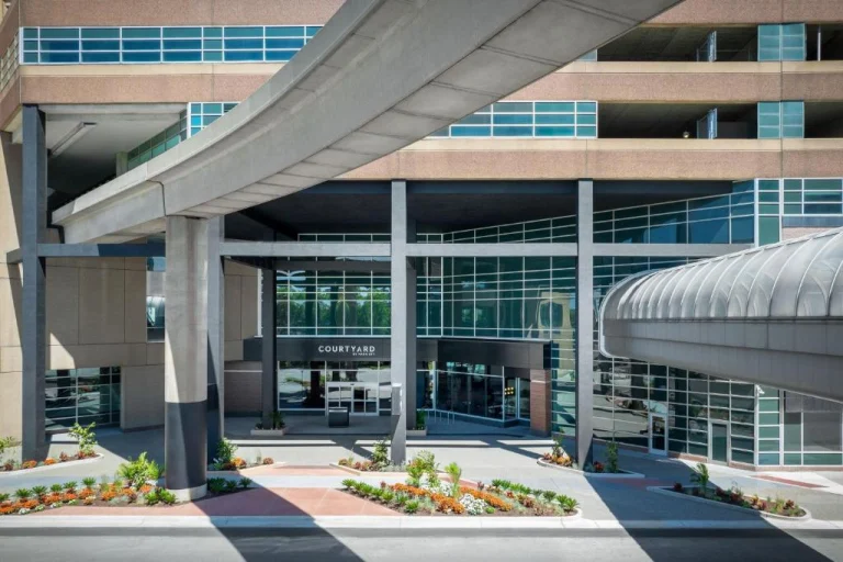 Betonnen hotelgebouw van Courtyard met een gebogen overdekte loopbrug naar de ingang bij een luchthaven in Michigan