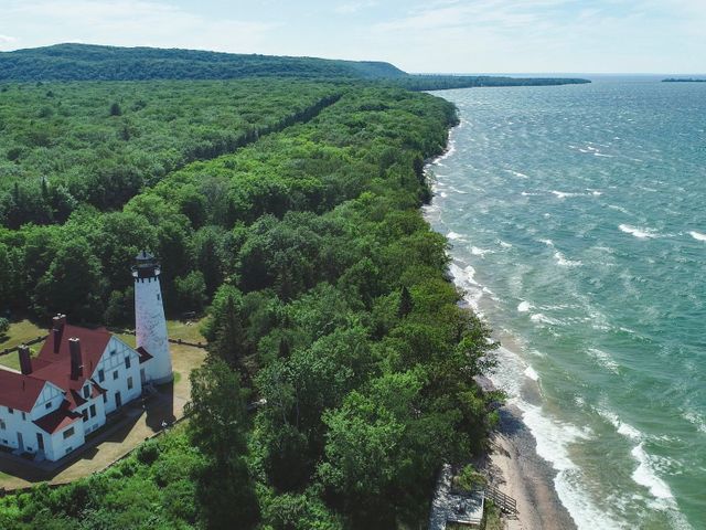 Luchtfoto van een witte vuurtoren met rood dak langs een beboste kustlijn met golvend water van Lake Superior in Michigan