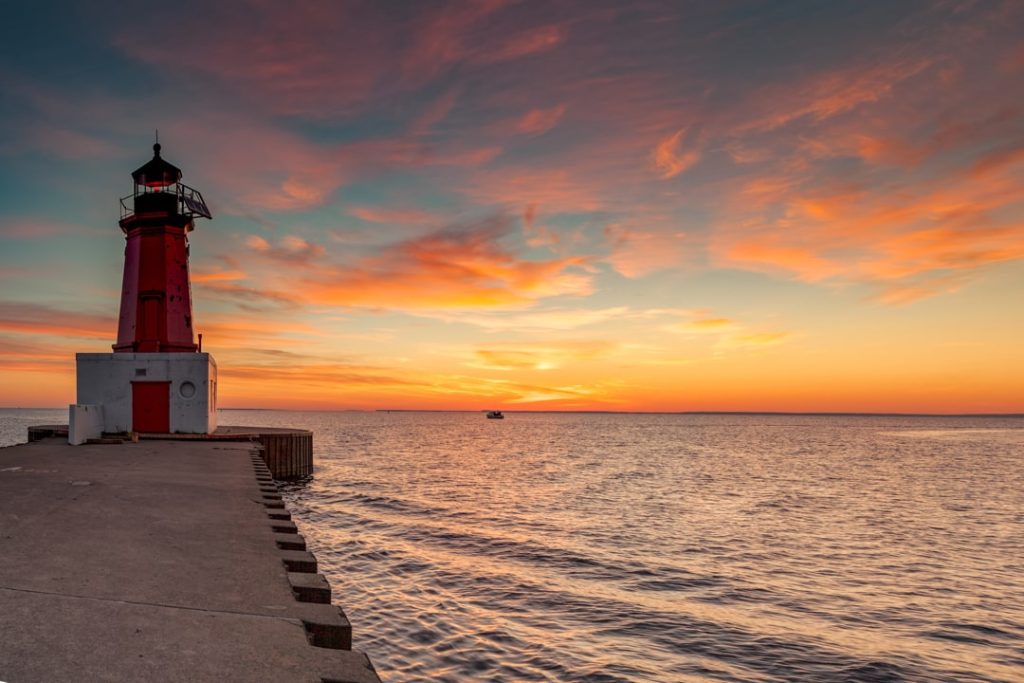 Rode witte vuurtoren aan het einde van een lange pier, met een kleurrijke oranje en blauwe zonsondergang boven het water