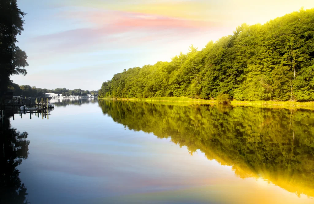 Stil wateroppervlak van een rivier dat de bosrand en een roze avondlucht weerspiegelt in Michigan met aangemeerde boten in de verte