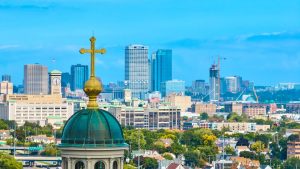 Groene koepel van een basiliek met een gouden kruis op de voorgrond, met de wolkenkrabbers van Milwaukee op de achtergrond onder een blauwe lucht